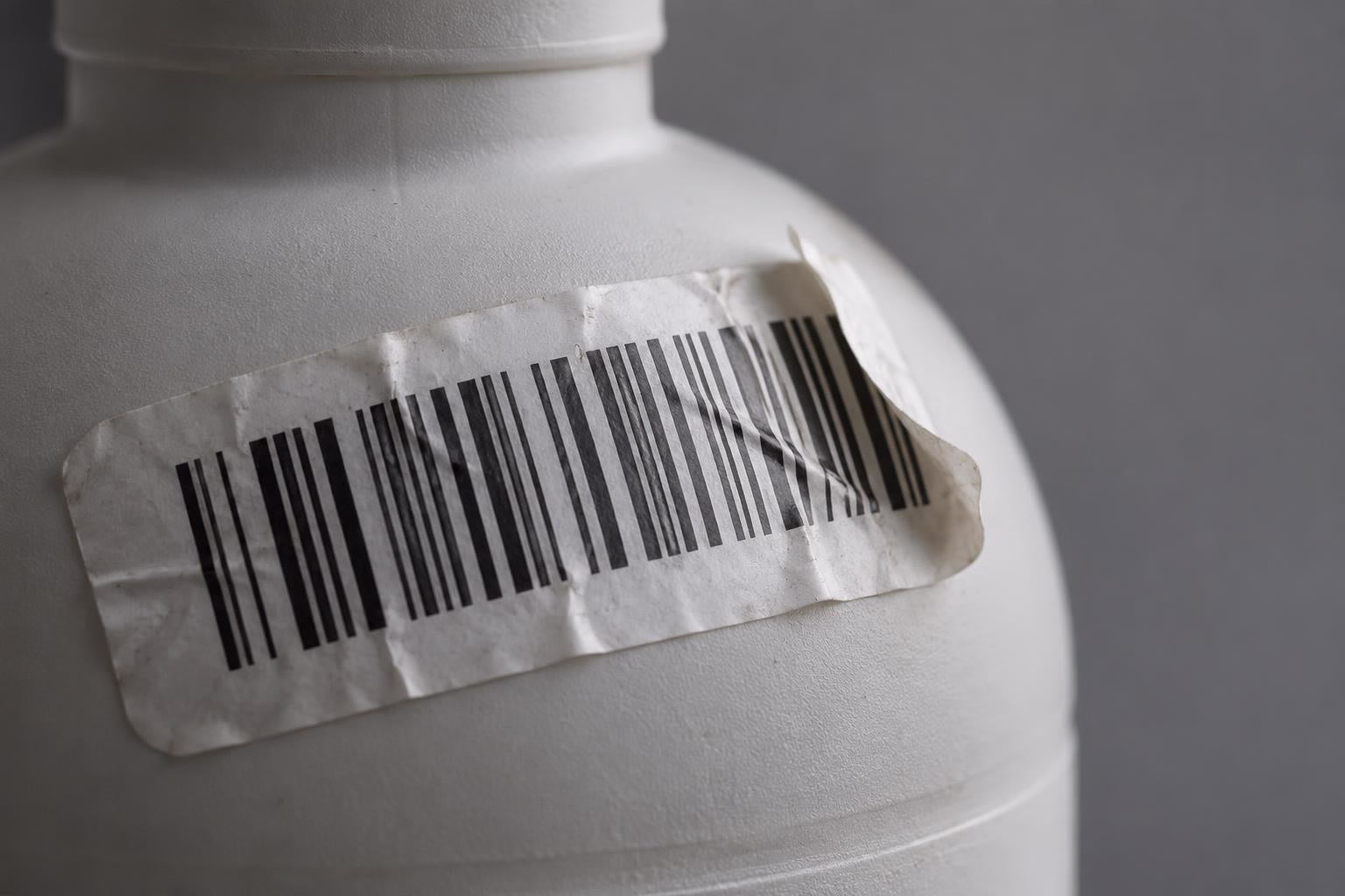 Een verkreukeld barcode-etiket laat los van de ronde schouder van een plastic fles